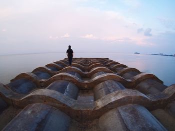 Man walking on pier over sea against sky during sunset