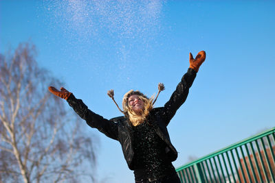 Happy young woman throwing snow against clear blue sky