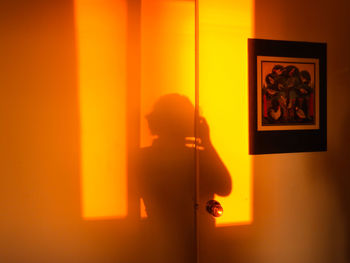 Reflection of man photographing illuminated lamp on wall at home