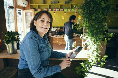 Portrait of happy owner sitting with digital tablet in cafe