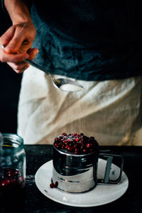Midsection of man pouring sugar on cranberries