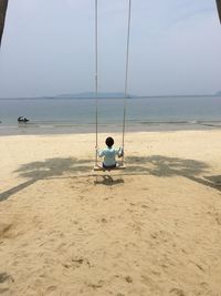 Man fishing on swing at beach against sky