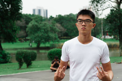 Portrait of young man gesturing peace sign while standing against trees