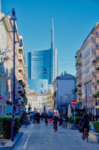 People on street amidst buildings in city against clear blue sky