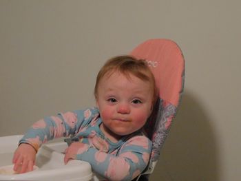 Portrait of cute baby girl relaxing on chair against wall