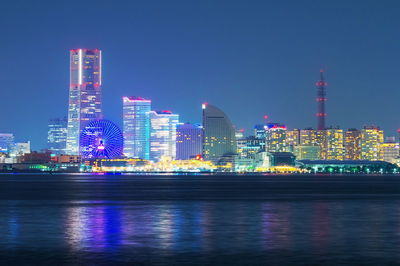 Illuminated buildings by river against sky at night