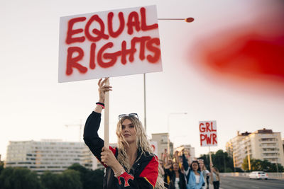 Women protesting with friends for equal rights in city against sky