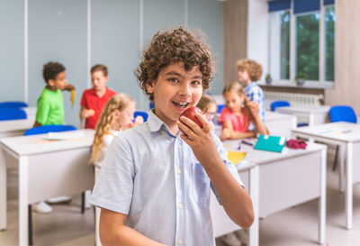 Portrait of boy eating apple at classroom