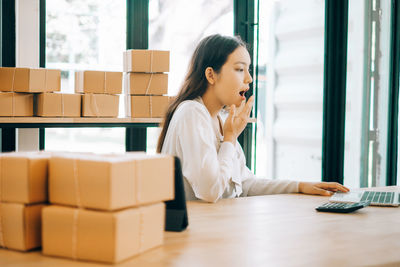 Side view of young woman using phone while sitting on table