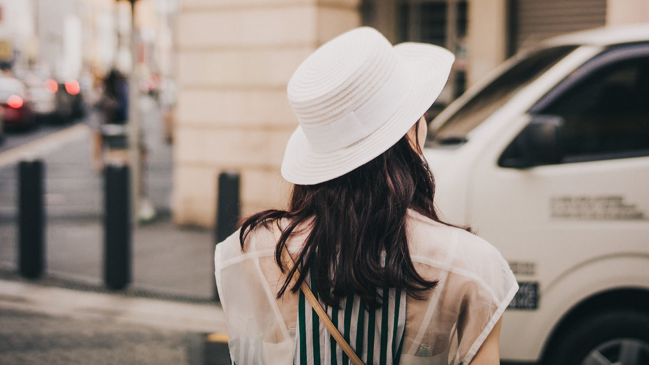 one person, real people, rear view, women, hat, focus on foreground, lifestyles, adult, clothing, leisure activity, city, motor vehicle, transportation, headshot, standing, mode of transportation, land vehicle, car, hairstyle