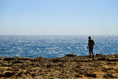 Rear view of man standing on beach against clear sky