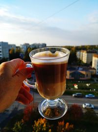 Close-up of hand holding coffee cup against sky