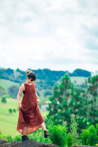 Side view young woman wearing sunglasses walking on mountain against cloudy sky