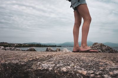 Low section of woman standing on rock against sky