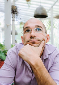 Attractive adult man with glasses holds his chin with the hand and looking up in a pensive mood.