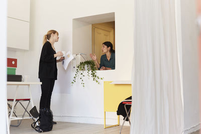 Businesswoman standing at window while discussing with colleague in office