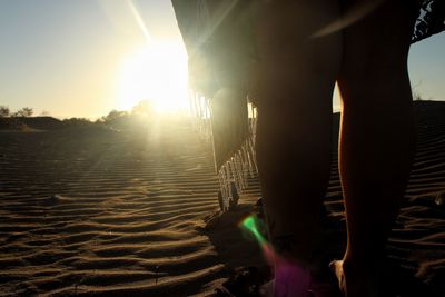 Rear view of man standing at beach against sky during sunset