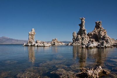 View of rock formation in sea against clear blue sky