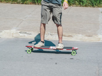 Low section of man skateboarding on road during sunny day