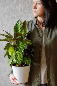  woman with dark hair in a green shirt holds in her hands a beautiful calathea flower in a white pot