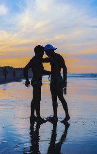 Silhouette friends standing at beach against sky during sunset