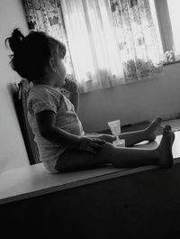 Side view of girl sitting on book at home