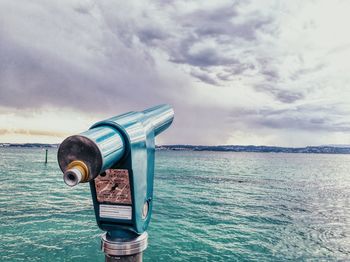 Close-up of coin-operated binoculars by sea against sky