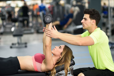 Trainer assisting woman exercising in gym