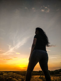 Low angle view of woman standing against sky during sunset