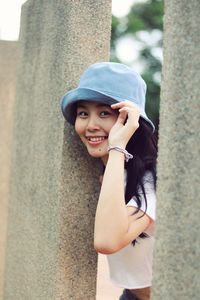 Portrait of smiling young woman standing against pillar