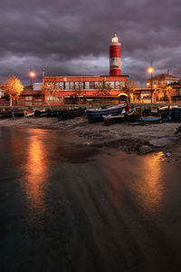 Illuminated buildings by sea against sky at night