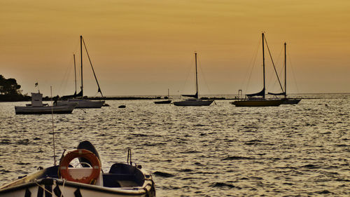 Sailboats moored on sea against sky during sunset