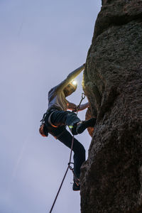 Side view of sportive male alpinist ascending on cliff in mountain terrain in cloudy day