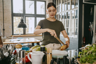 Young female chef adding chickpeas in pan while preparing food at studio