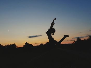 Silhouette person with arms raised against sky during sunset