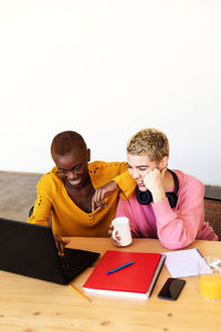 Cheerful lesbian couple working over laptop on table at home