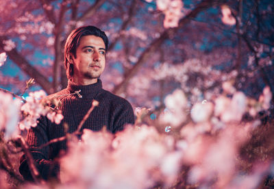 Young man looking away by cherry tree at night