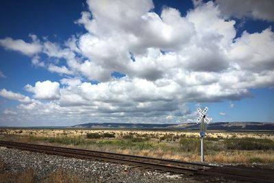 Sign board with text by railroad track against sky