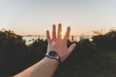 Cropped image of hand wearing wristwatch at lakeshore during sunset