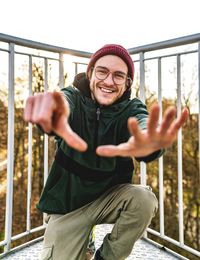 Portrait of smiling young man standing against railing