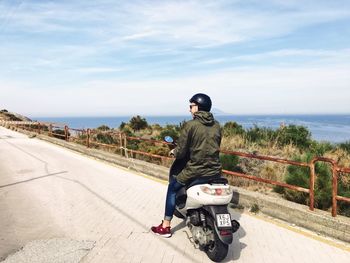 Rear view of man sitting on motor scooter against sky