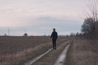 Rear view of man walking on field against sky