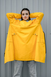 Girl in a yellow raincoat and gray jeans stands on a gray background. youth subculture