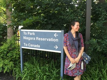 Smiling woman standing by information sign in forest