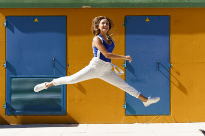 Full length of smiling woman jumping against yellow wall