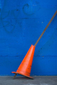 Broken traffic cone on sidewalk against blue wall