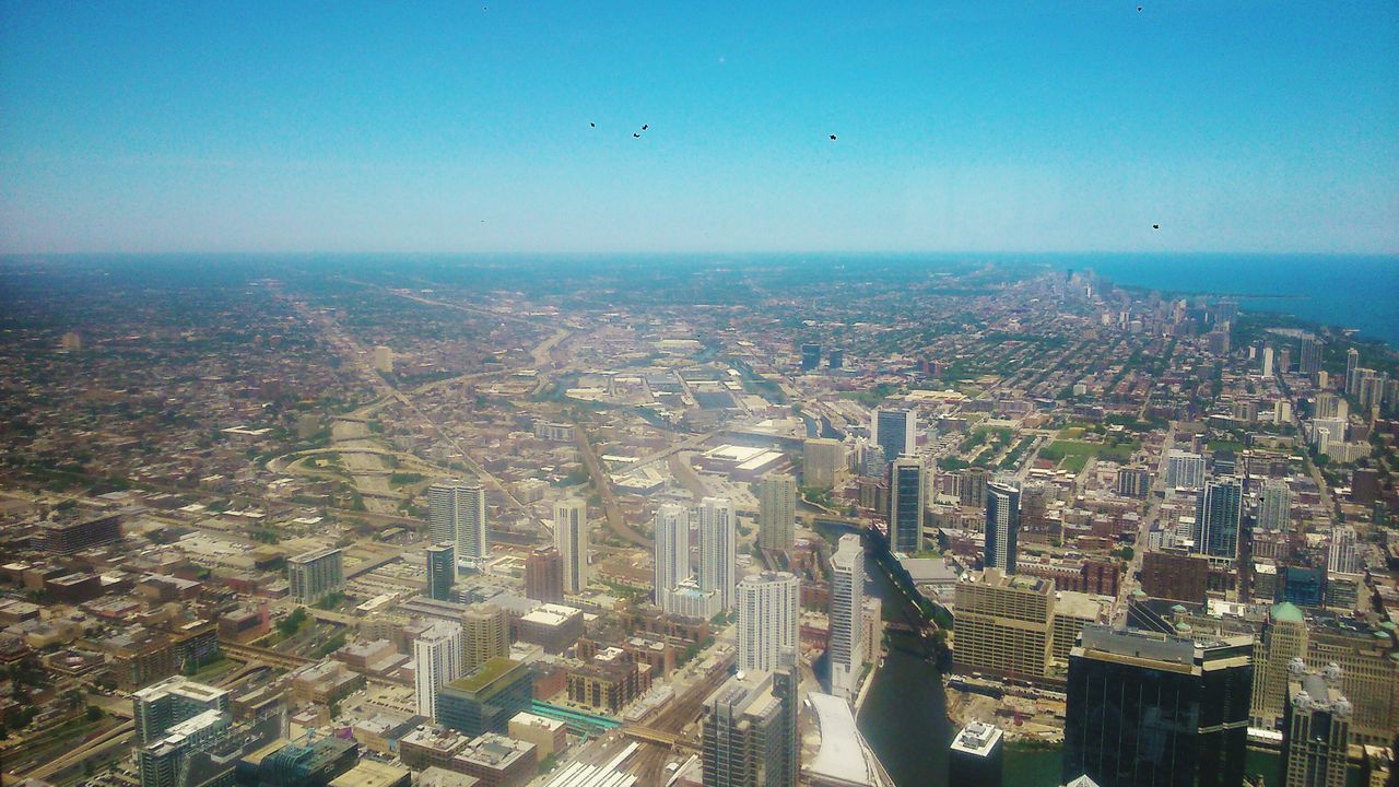 cityscape, architecture, city, building exterior, built structure, flying, aerial view, crowded, high angle view, clear sky, blue, skyscraper, residential district, mid-air, sea, modern, sky, city life, capital cities, residential building