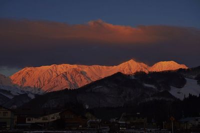 Buildings by snowcapped mountains against sky during sunrise