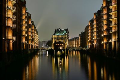 Panoramic view of river amidst illuminated buildings in city at dusk