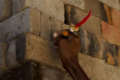 Close-up of hand holding dry leaf against wall